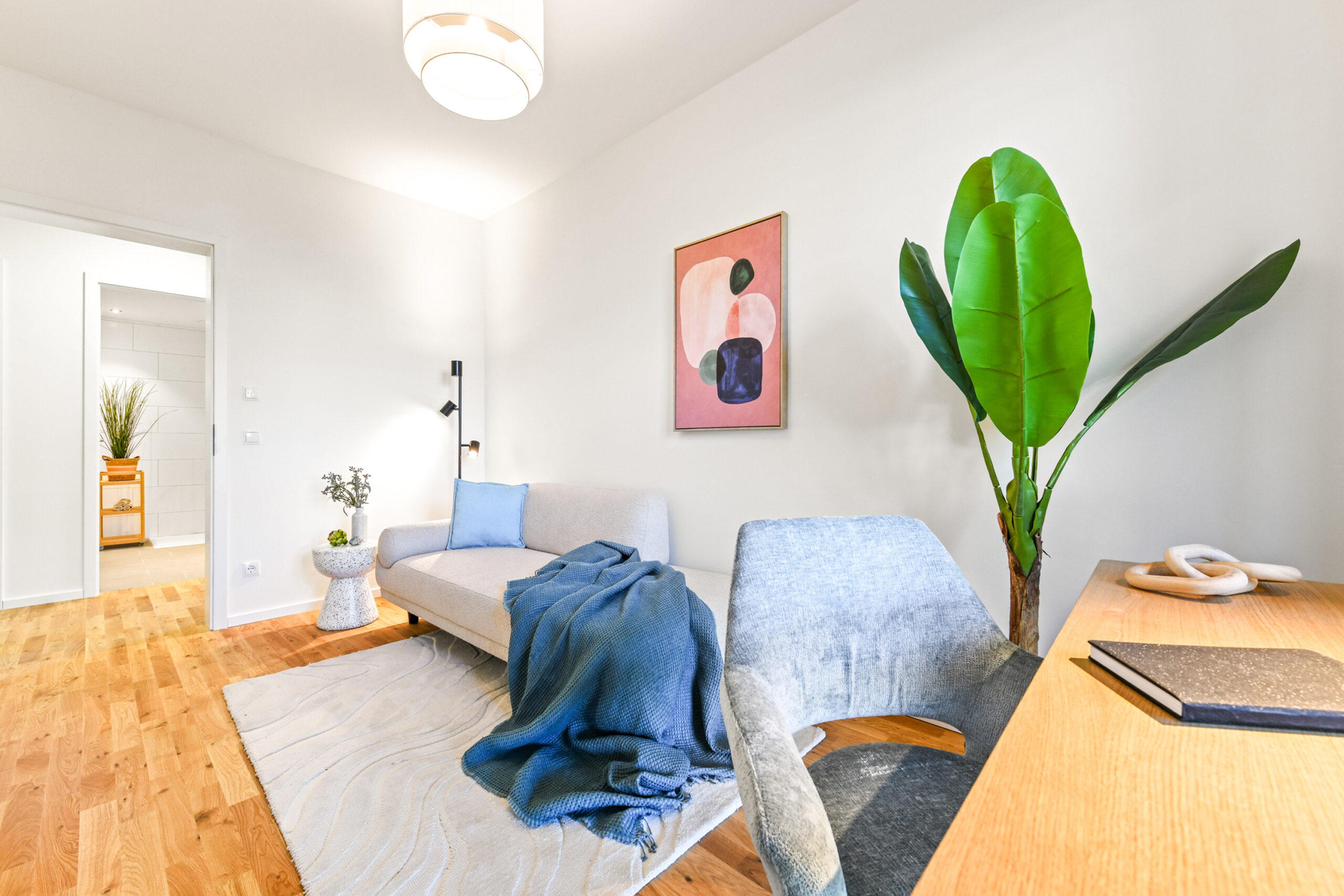 Helles Wohnzimmer mit Sofa, Schreibtisch, Pflanze und modernem Wandbild.