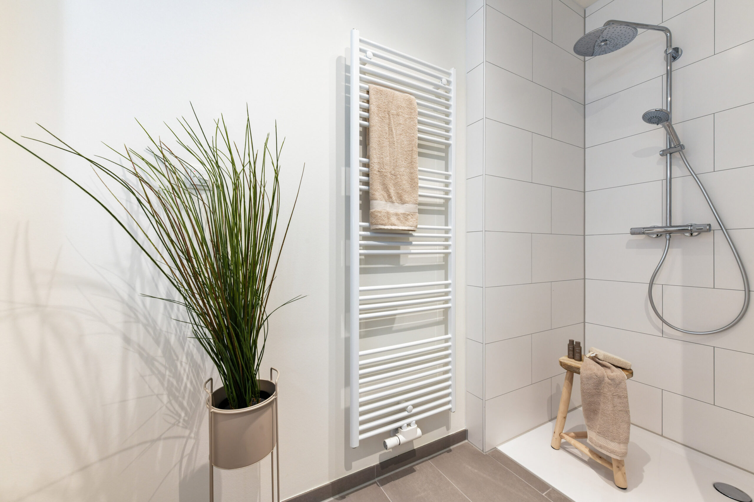 Modernes Bad mit begehbarer Dusche, Handtuchheizung, Hocker und Pflanze.