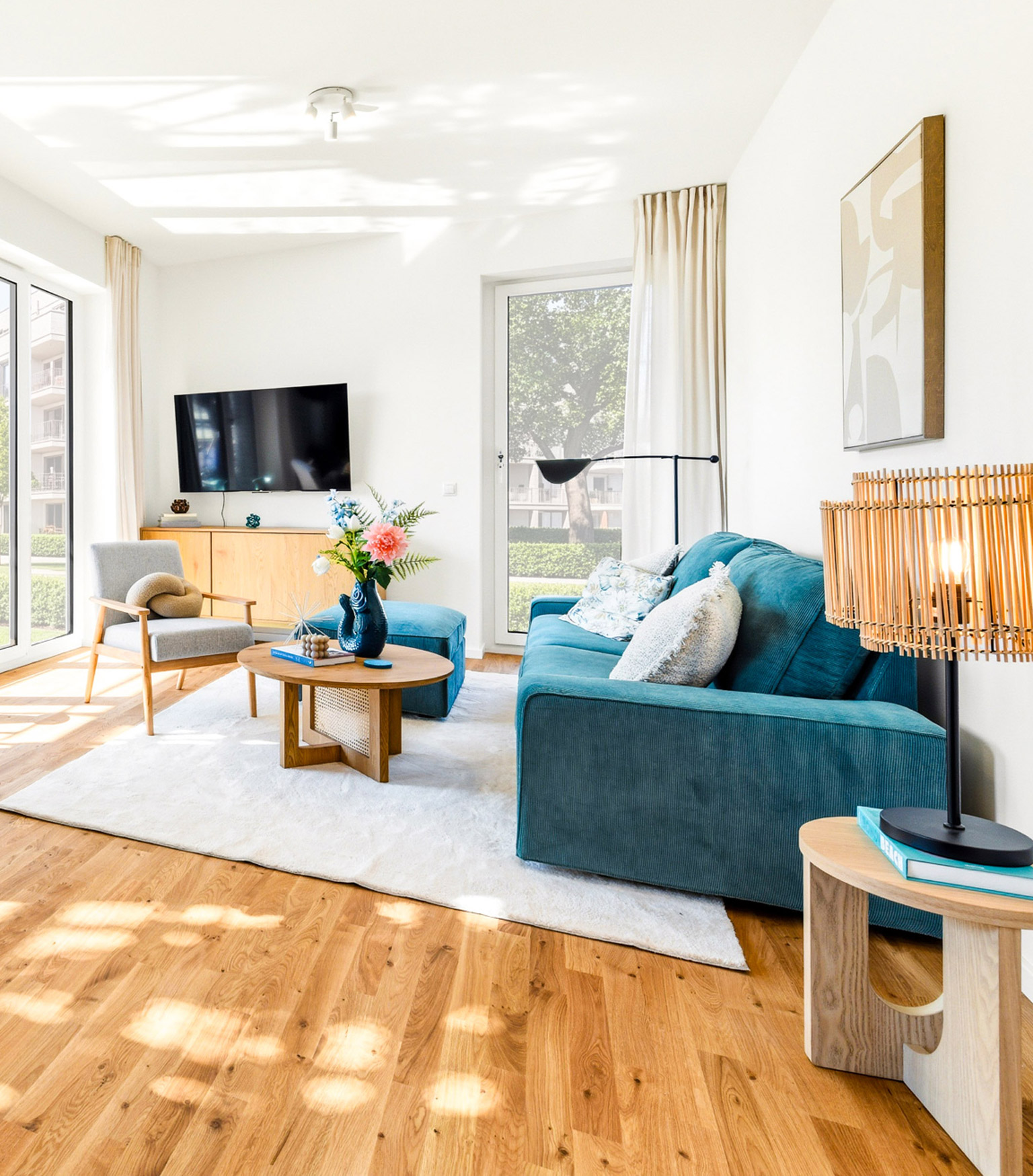 Helles Wohnzimmer mit blauem Sofa, Holzmöbeln und großen Fenstern.