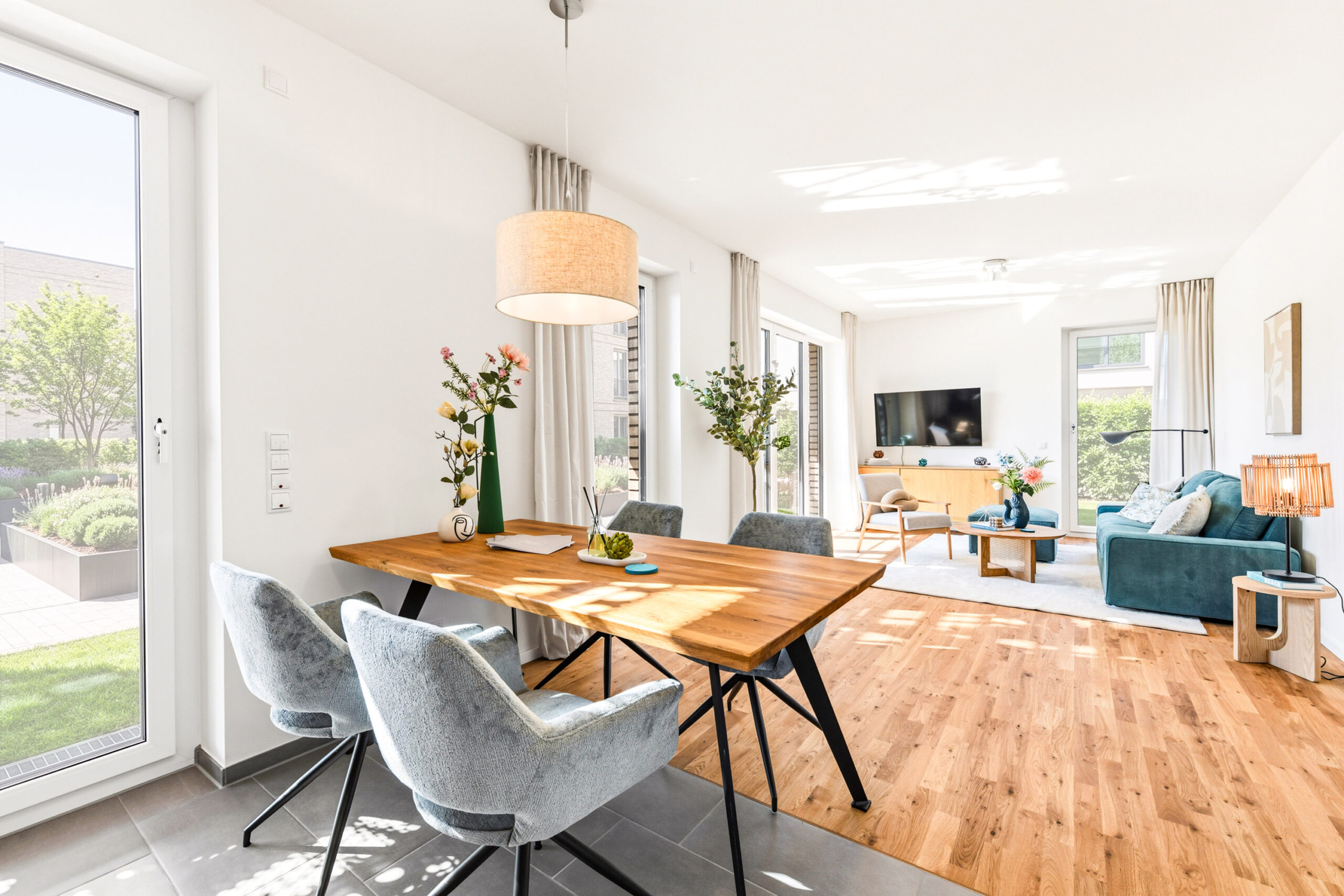 Helles Wohn- und Esszimmer mit Holzboden, großen Fenstern und moderner Einrichtung.