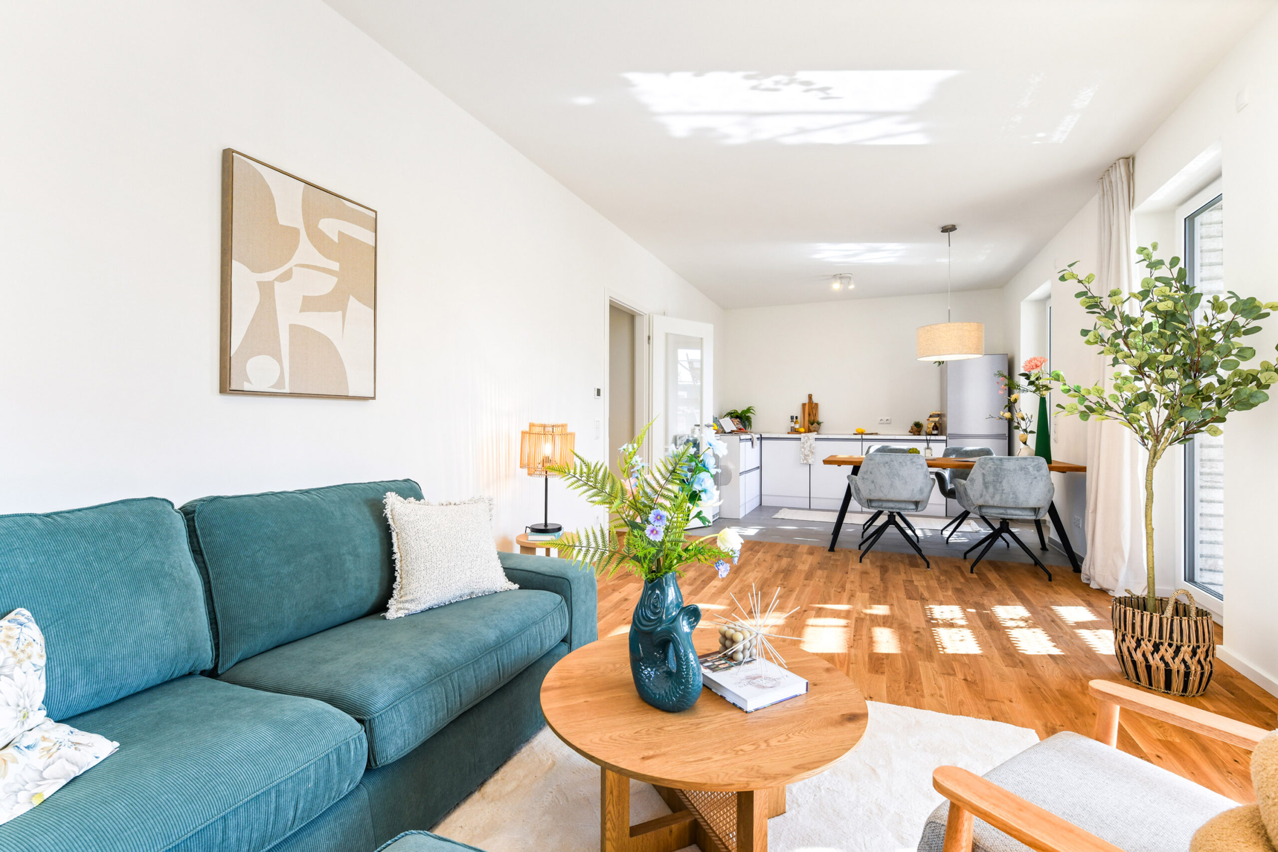 Helles Wohnzimmer mit grüner Couch, Holztisch, Pflanzen und Blick zur Küche.